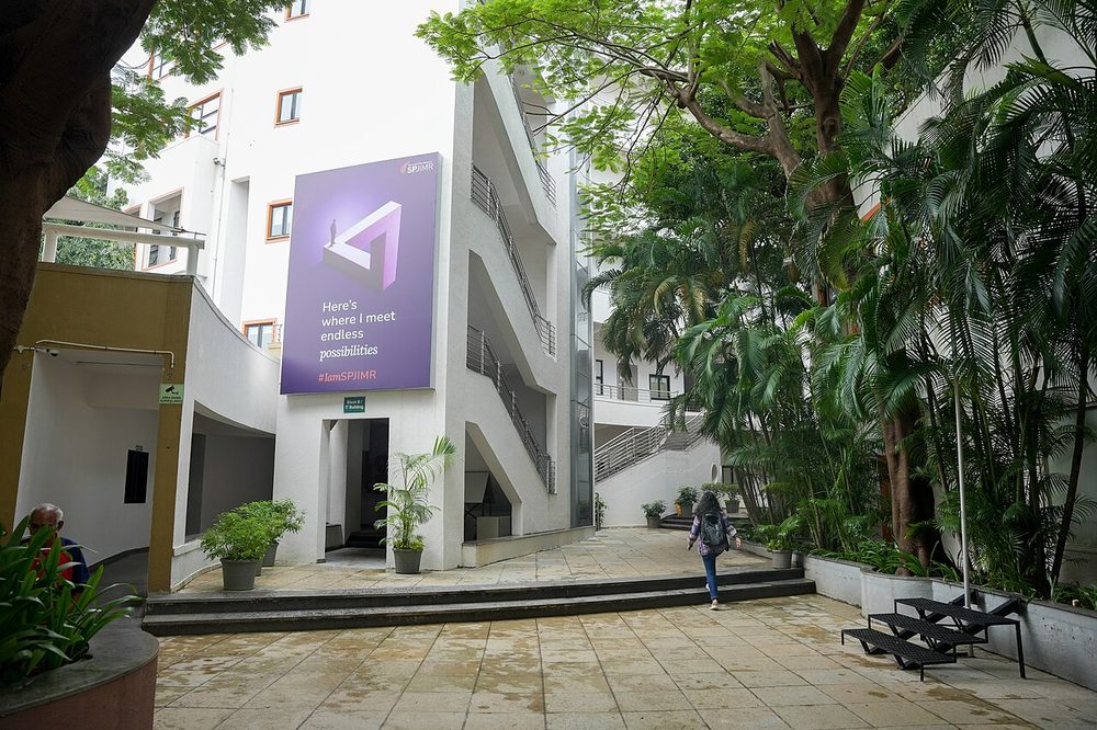 Students walking past a campus entrance surrounded by trees